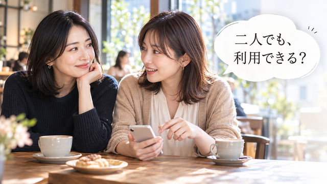 カフェでスマートフォンを見ながら顔を見合わせて話す女性二人