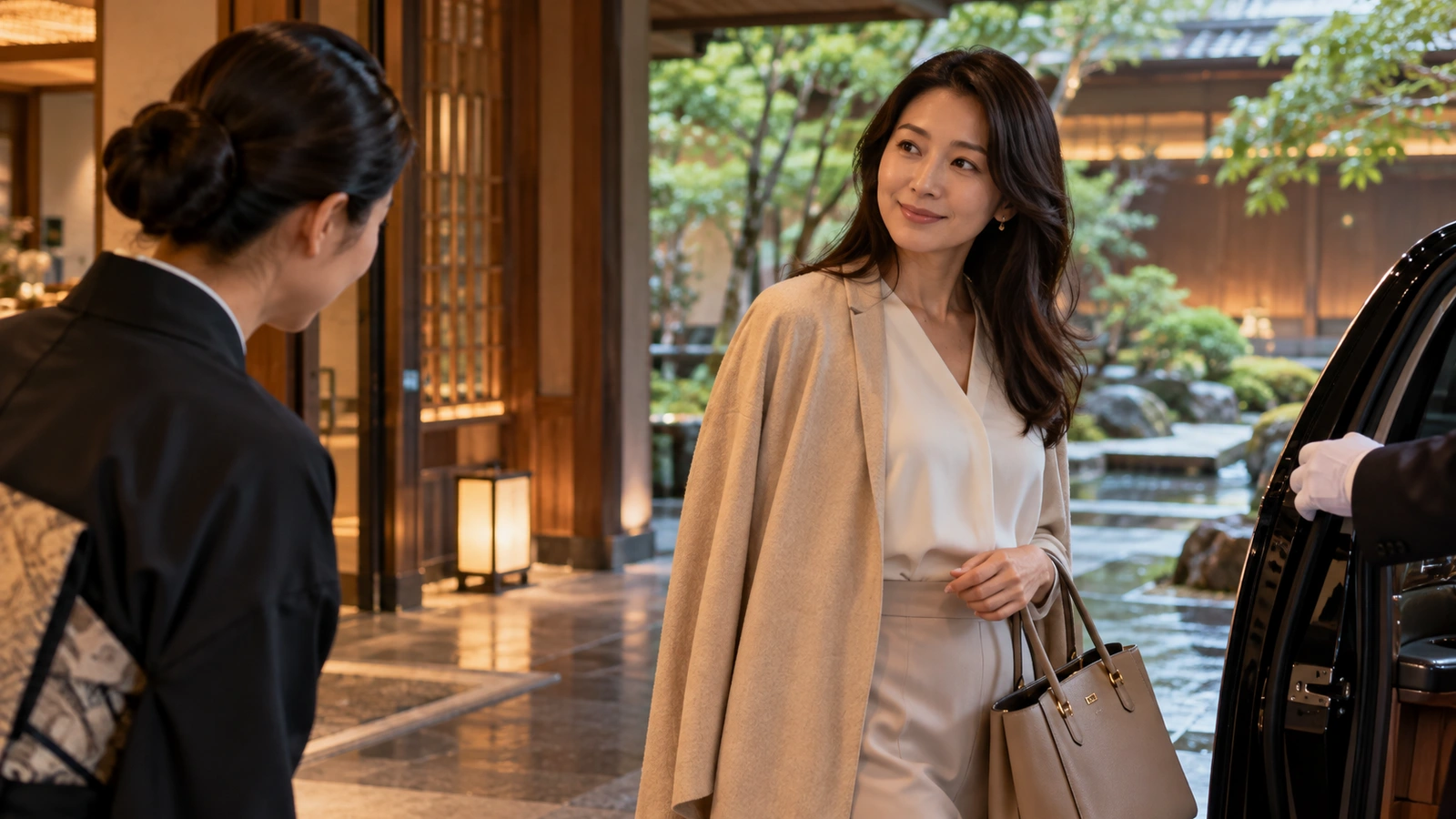 A woman with a shoulder bag looks back while walking beneath warm lighting near a hotel driveway and entrance; a dark handbag is visible beside her.