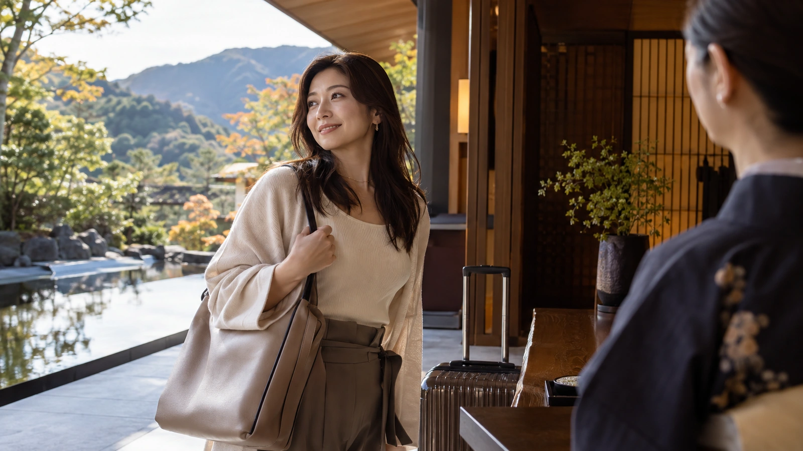 A woman with a shoulder bag looks back while walking in a lakeside hotel lobby overlooking wooded hills; a wheeled travel case is beside her.
