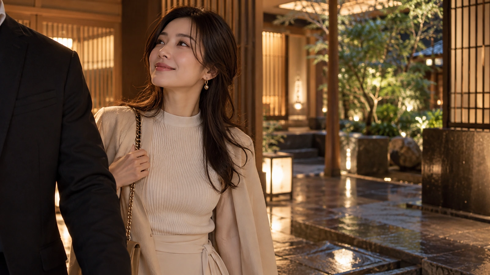 一名女性行走時回頭望向畫面邊緣穿西裝的同行者，場景是有石徑、植栽與低矮燈籠的日式池畔；身邊可見一只深色手提包。